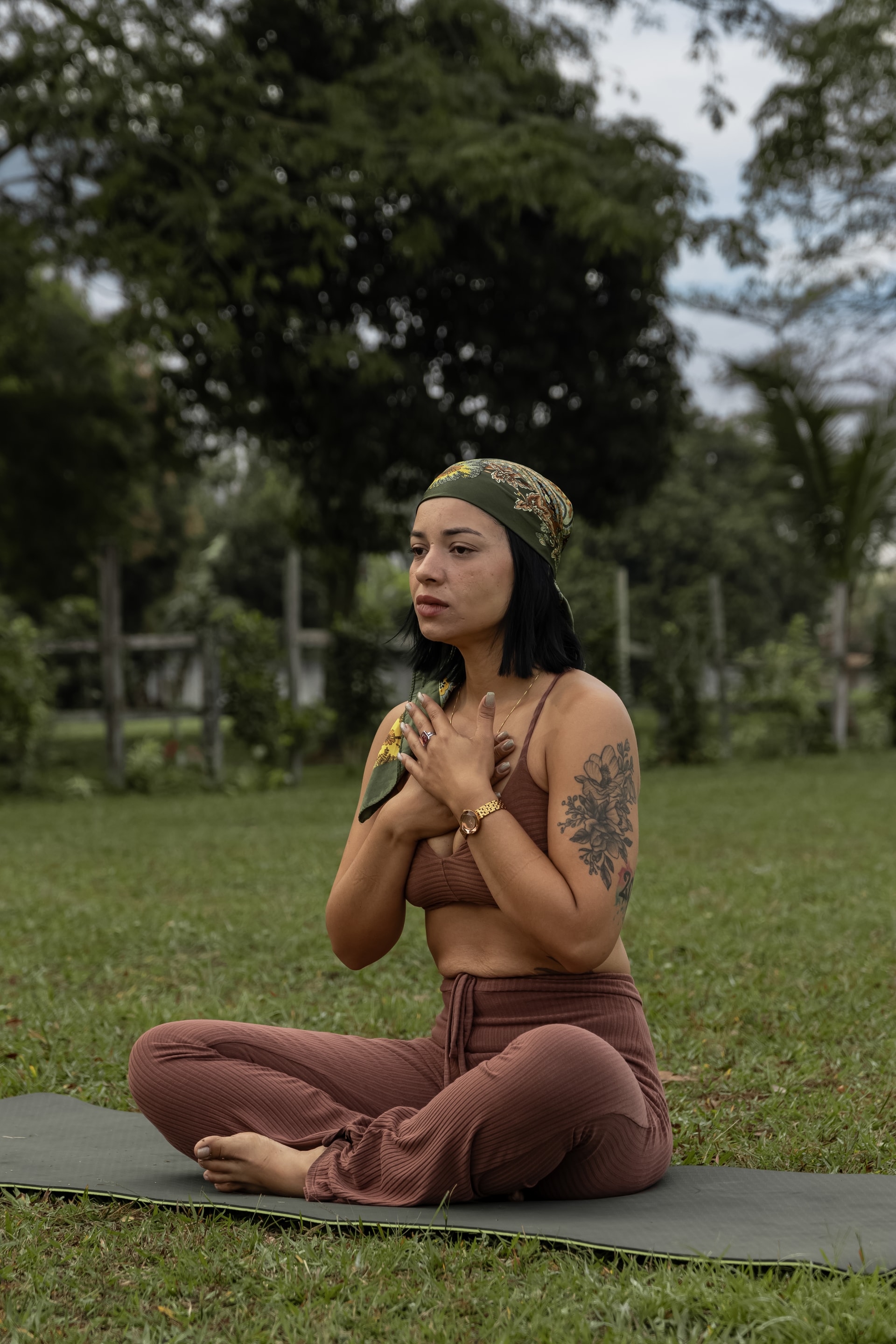 Mulher sentada sobre um tapete com as mãos junto ao peito