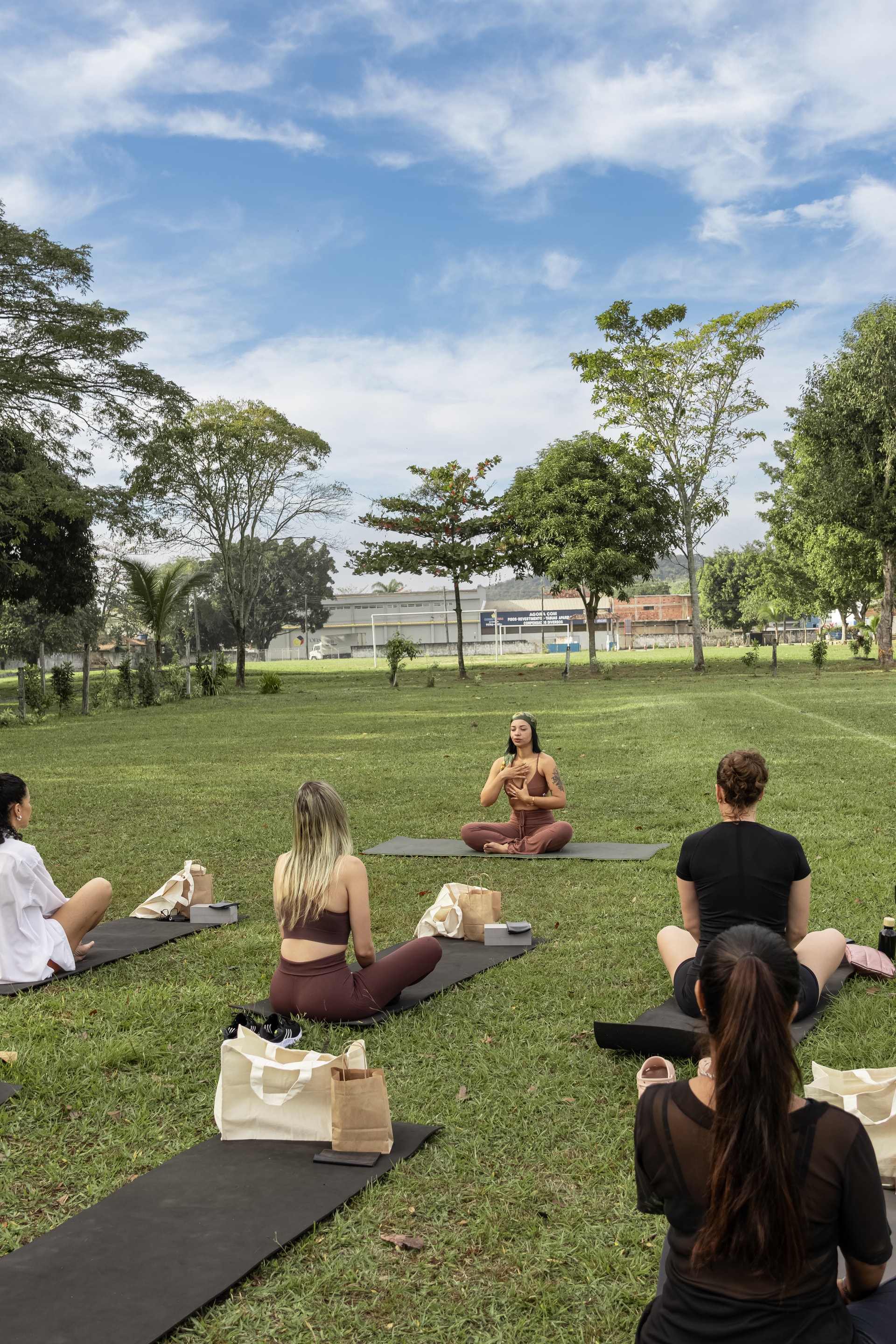 Grupo sentado em tapetes diante de uma facilitadora no campo